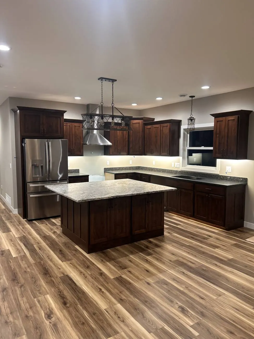 Kitchen with dark cabinets, recessed cans, linear island fixture and under-cabinet lighting