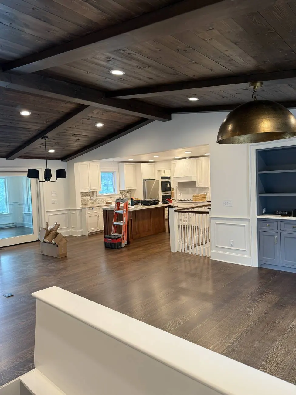 Open kitchen and dining area with stained beamed wood ceiling and brass dome pendant